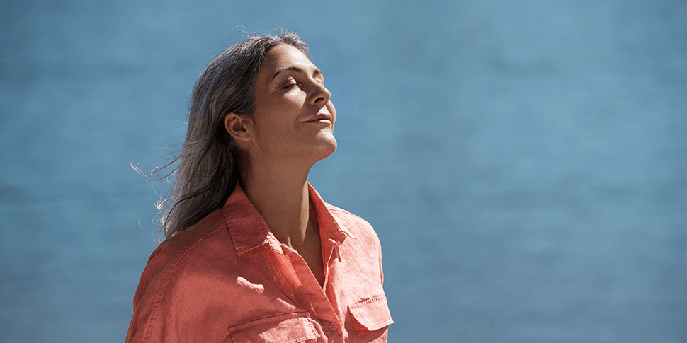 A smiling, relaxed woman standing outdoors in the sunshine