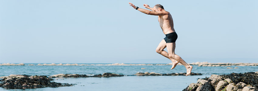 Senior male jumping into beach water