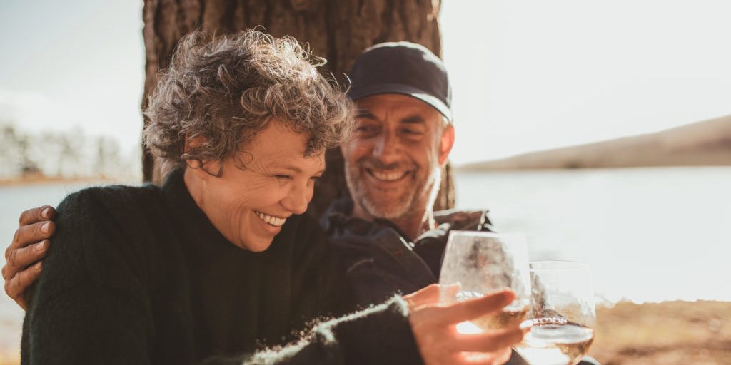 Portrait of relaxed mature couple having a glass of wine at campsite. Senior man and woman toasting wine at on summer day. Optimistic