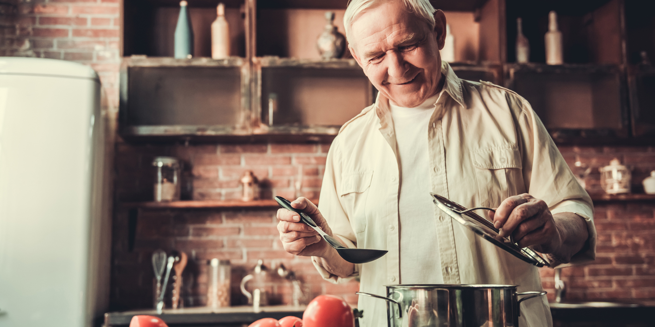 Handsome senior man is smiling while cooking in kitchen